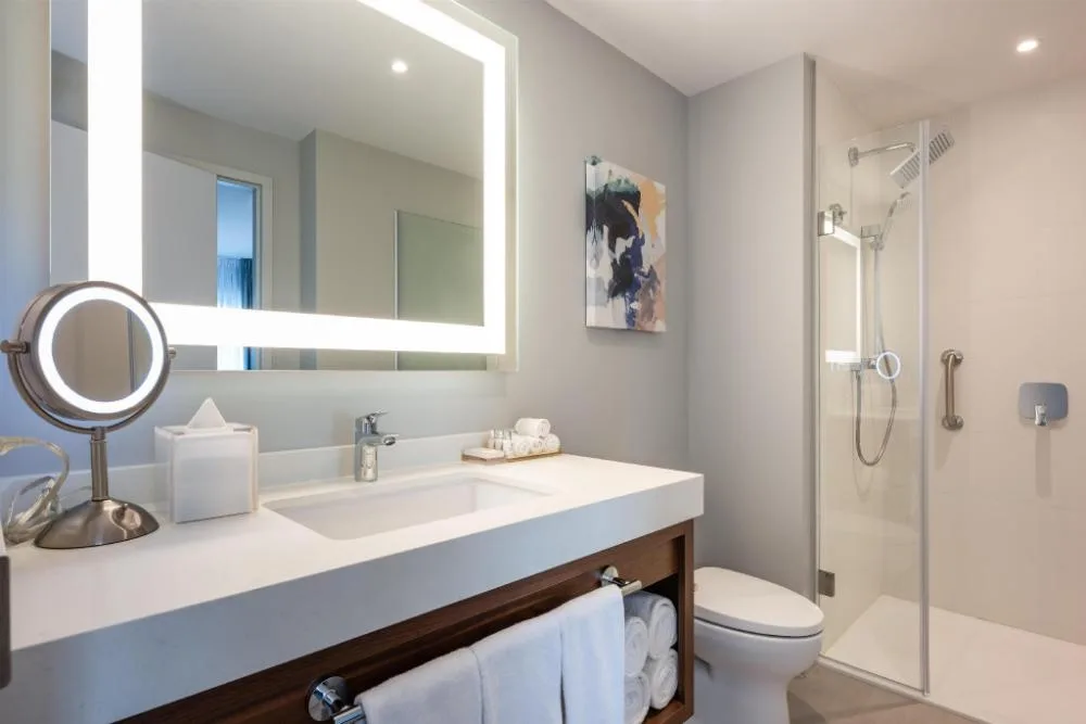 Suite bathroom with illuminated mirror and glass shower at Embassy Suites Aruba Beach Resort.