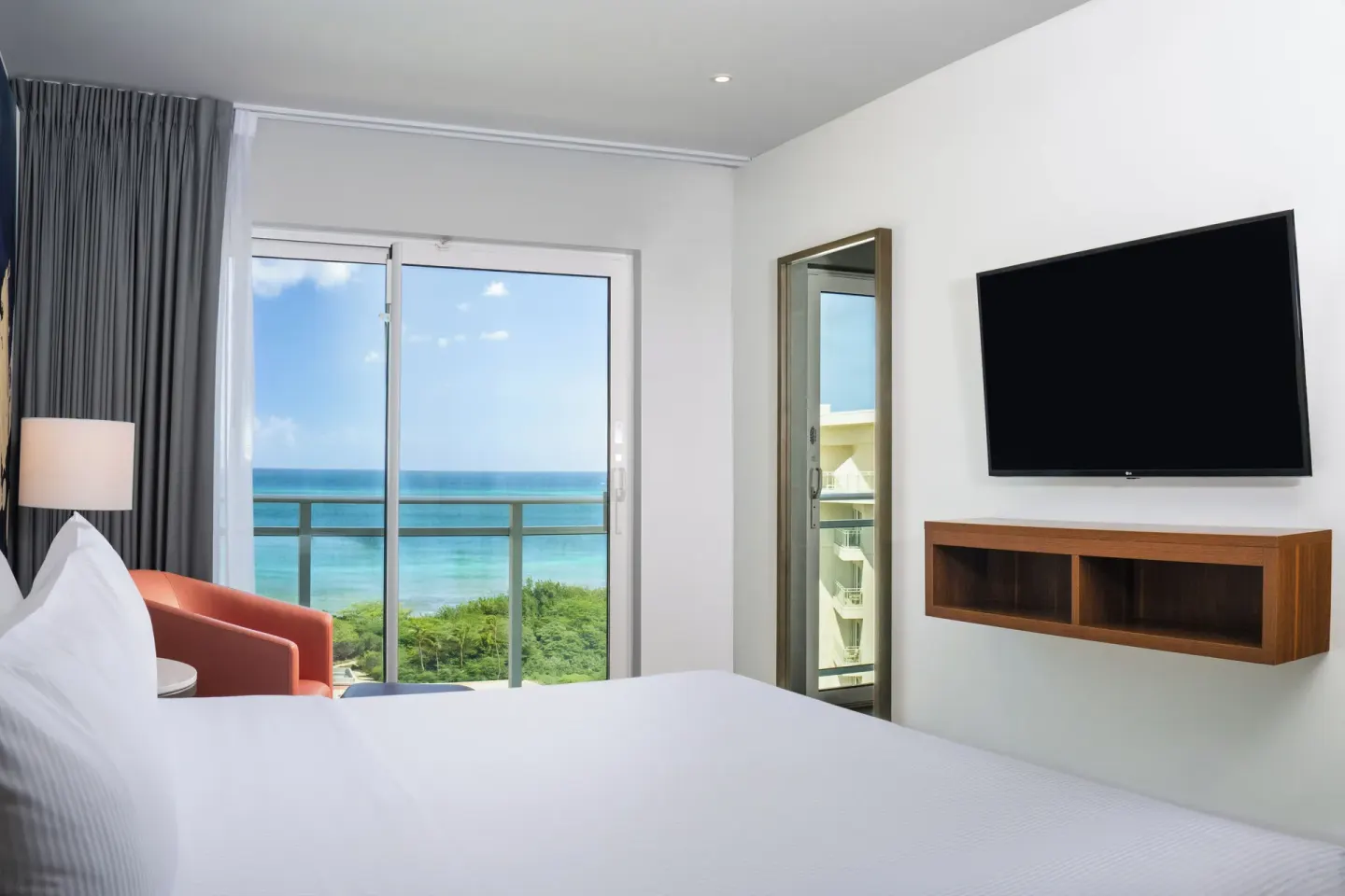 Ocean-view one-bedroom suite king bed facing balcony and TV at Embassy Suites Aruba Beach Resort.
