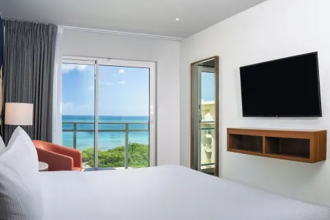 Ocean-view one-bedroom suite king bed facing balcony and TV at Embassy Suites Aruba Beach Resort.