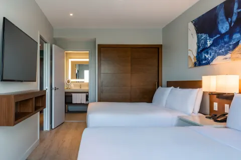 Two-bed bedroom with TV and bath entry at Embassy Suites Aruba Beach Resort.