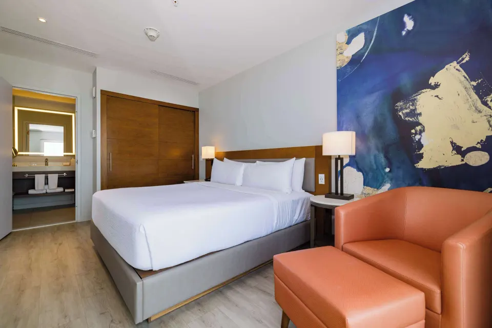 King bed suite with orange chair and bathroom at Embassy Suites Aruba Beach Resort.