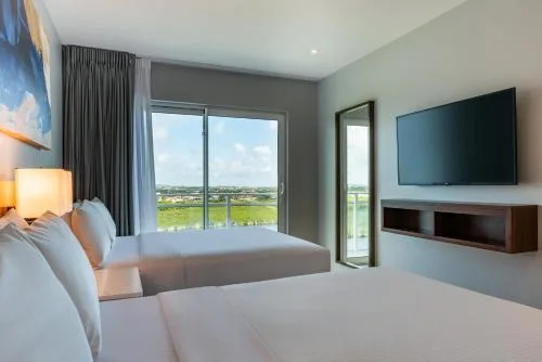 Bedroom with two beds, balcony doors and wall TV at Embassy Suites Aruba Beach Resort.