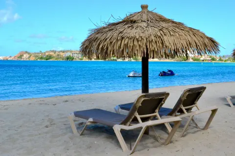 Beach loungers under a thatched umbrella face the bay at Emerald Beach Resort.