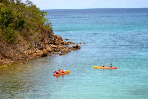 Kayakers paddle near a rocky shoreline by Emerald Beach Resort.