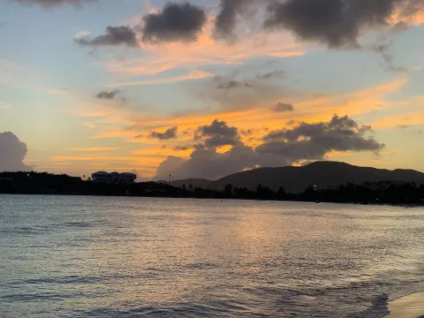 A colorful sunset glows over calm water and distant hills near Emerald Beach Resort.