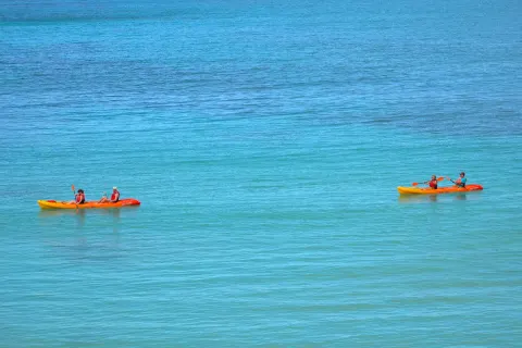 Two tandem kayaks glide across turquoise water at Emerald Beach Resort.