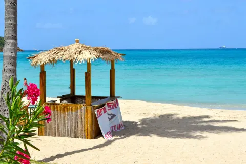 A thatched beach kiosk stands on white sand by turquoise water at Emerald Beach Resort.
