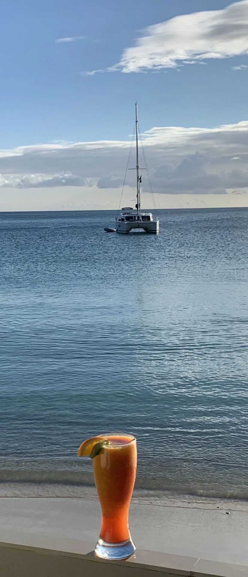 Orange tropical drink by the sea with a catamaran at Emerald Beach Resort.