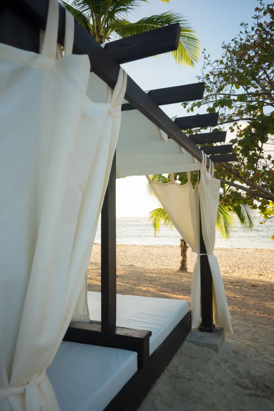 Beach cabana with white curtains facing the sea at Emotions by Hodelpa Puerto Plata.