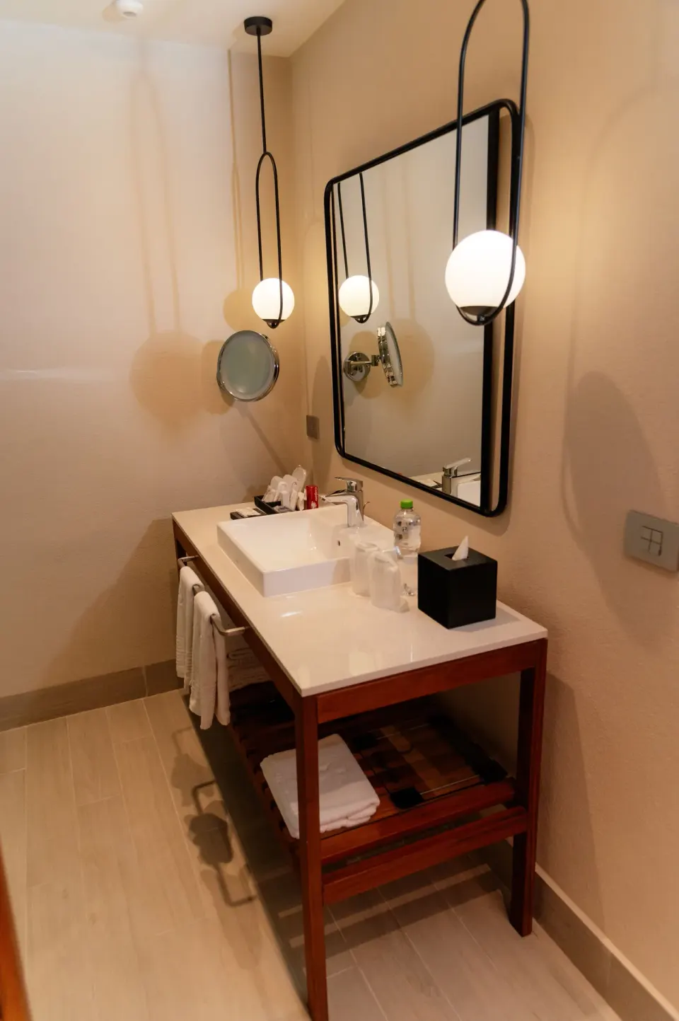 Bathroom vanity with round pendant lights, mirror, sink, towels, and tissue box at Emporio Cancun.
