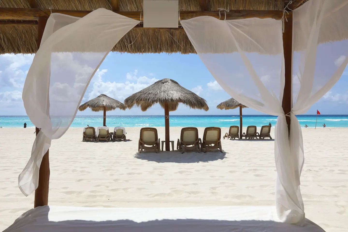 Beach cabana curtains frame loungers and palapas on the sand at Emporio Cancun.