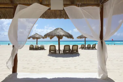Beach cabana curtains frame loungers and palapas on the sand at Emporio Cancun.