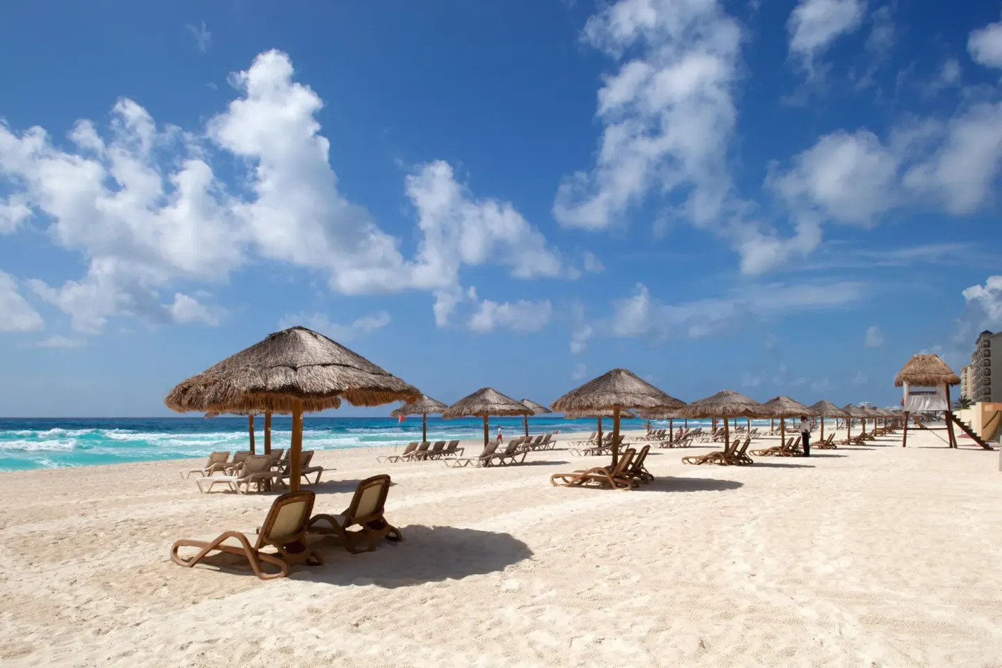 Beach with thatched umbrellas, lounge chairs, and turquoise sea at Emporio Cancun.