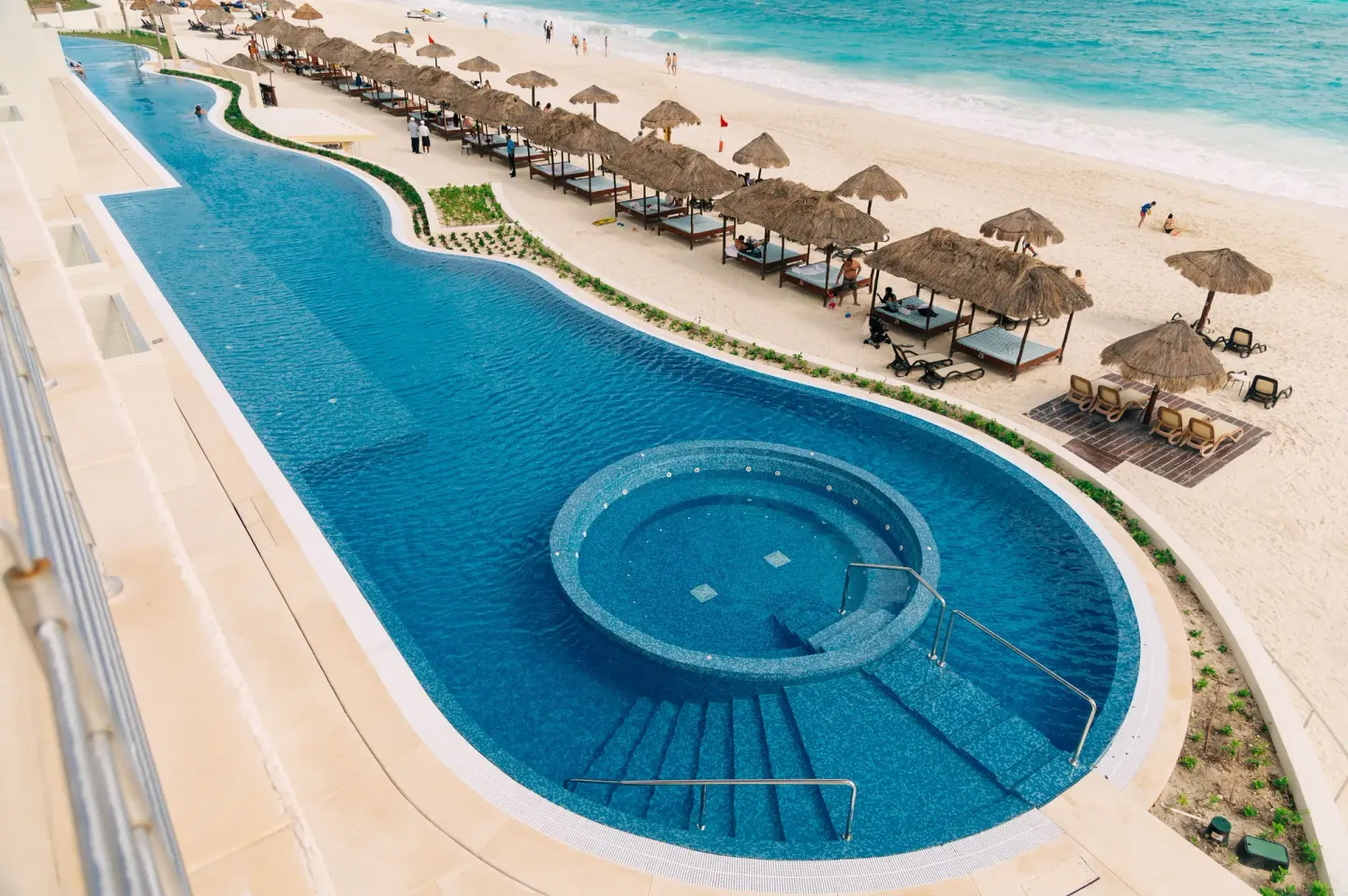 Beachfront pool with palapa cabanas and turquoise sea at Emporio Cancun.