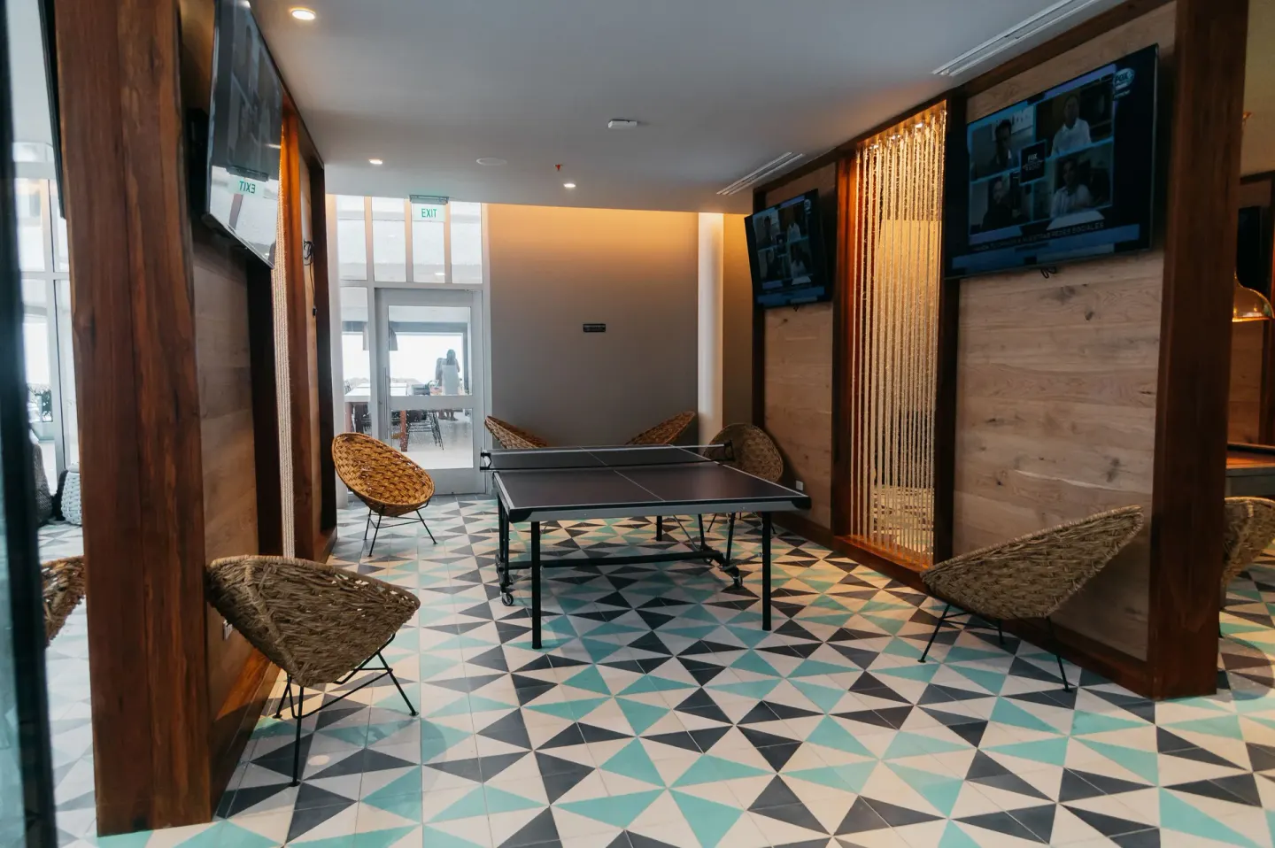 Game room with a ping-pong table, TVs, and woven chairs at Emporio Cancun.