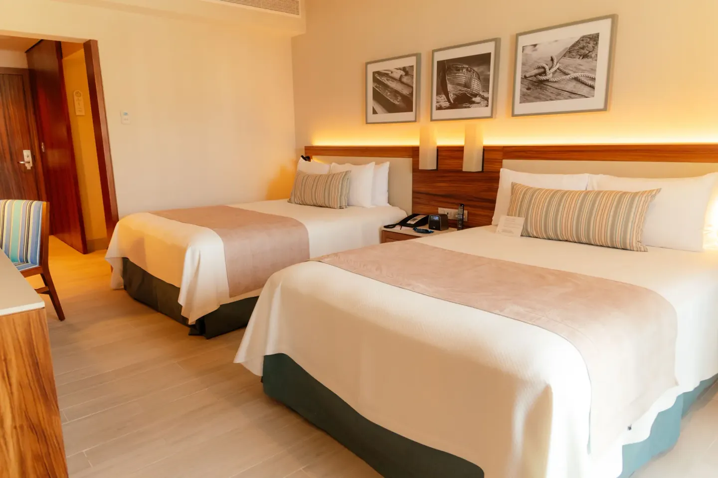 Guest room with two beds, warm headboard lighting, and framed art at Emporio Cancun.