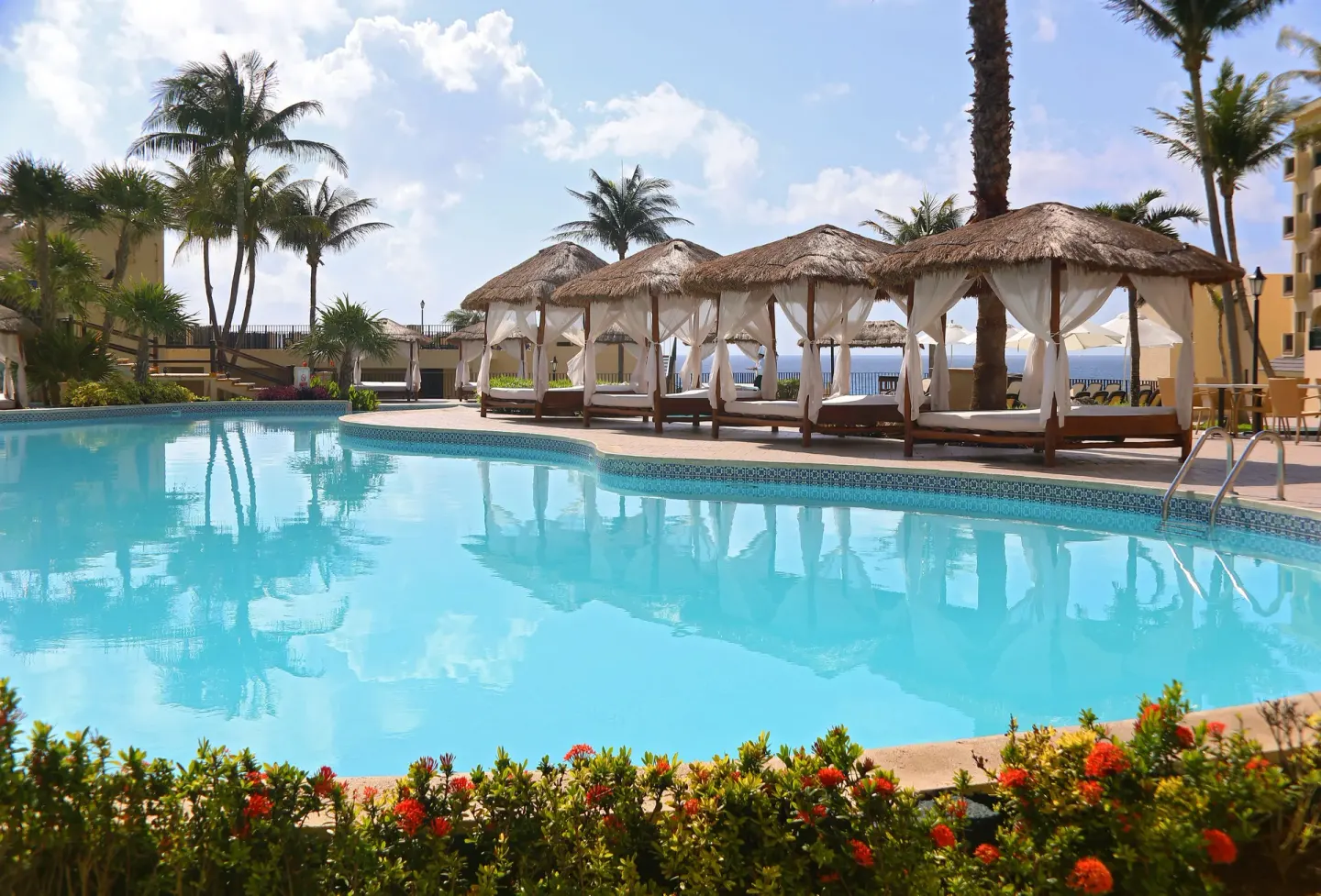Pool with cabanas, palm trees, flowers, and ocean glimpses at Emporio Cancun.