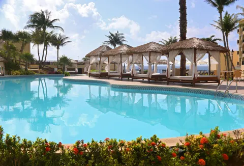 Pool with cabanas, palm trees, flowers, and ocean glimpses at Emporio Cancun.