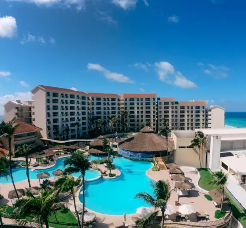Pool courtyard, palms, resort buildings, and ocean are seen from above at Emporio Cancun.