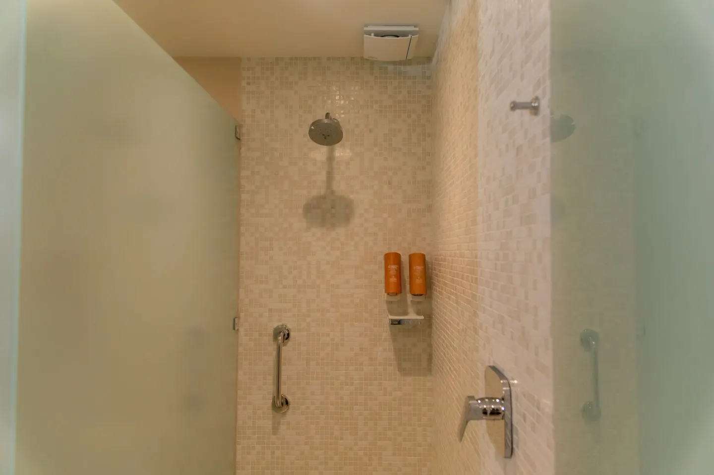 Walk-in shower with glass panels, mosaic tile, showerhead, and wall dispensers at Emporio Cancun.