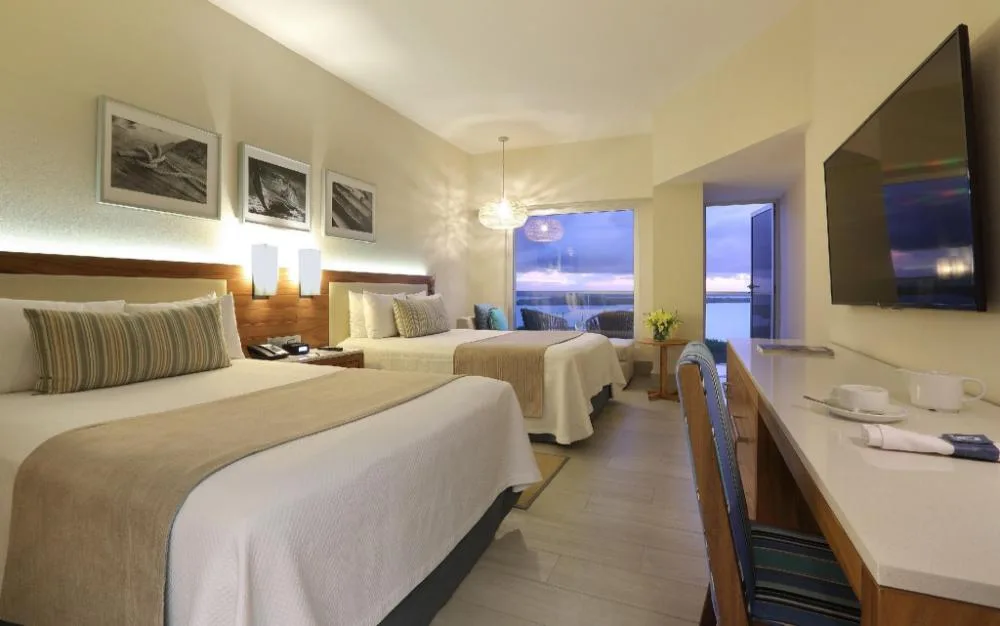 Deluxe Ocean Front room with two beds, desk, TV, and evening ocean view at Emporio Cancun.