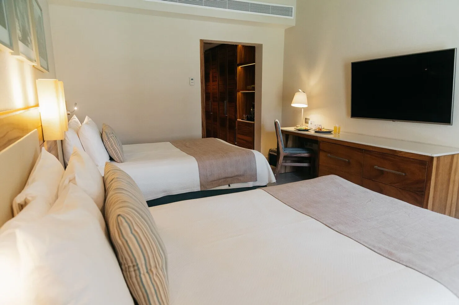 Super Saver room with two beds, desk, wall-mounted TV, and open closet at Emporio Cancun.