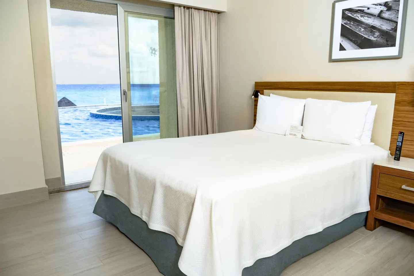 White bed in a Swim Up Oceanfront room at Emporio Cancun beside sliding doors to the oceanfront terrace.