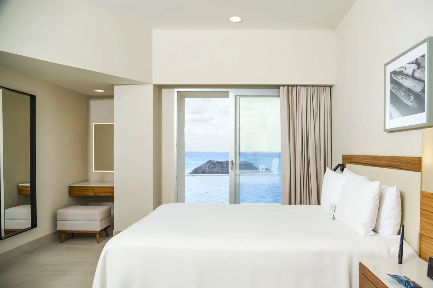 King bed in a Swim Up Oceanfront room at Emporio Cancun with vanity nook and ocean beyond the glass doors.