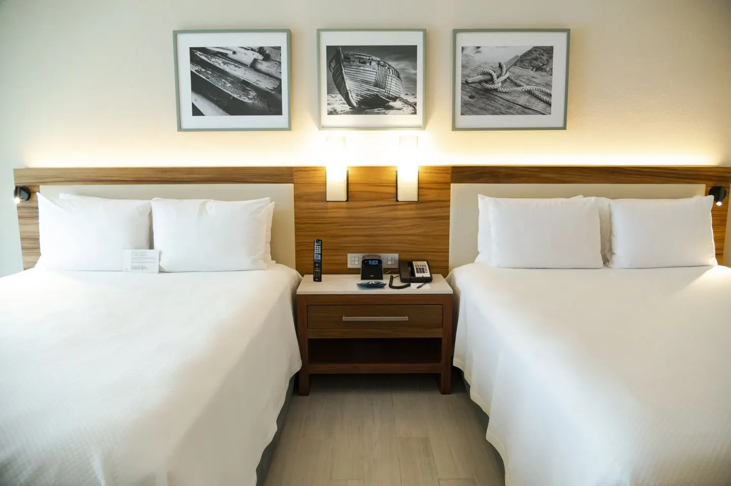 Two white beds in a Swim Up Oceanfront room at Emporio Cancun with nightstand and coastal wall art.