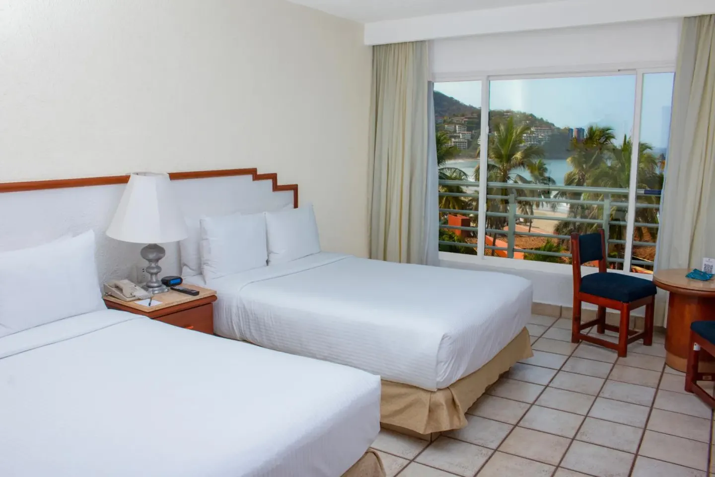 Double-bed guest room with window overlooking palms and bay at Emporio Ixtapa.