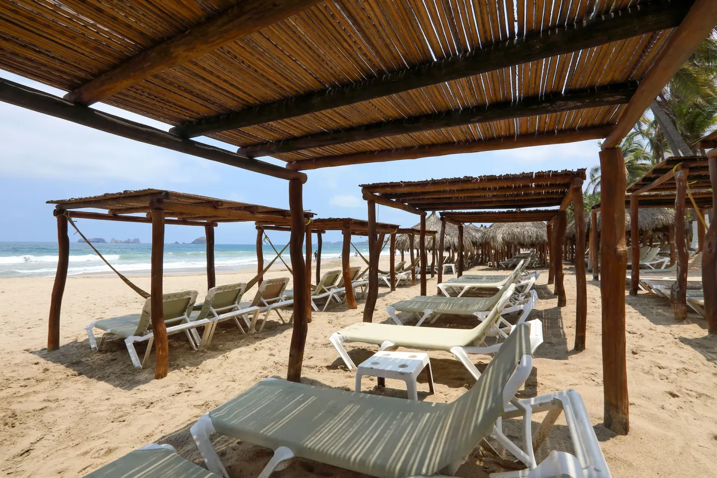 Beach loungers under wooden shade structures on the sand at Emporio Ixtapa.