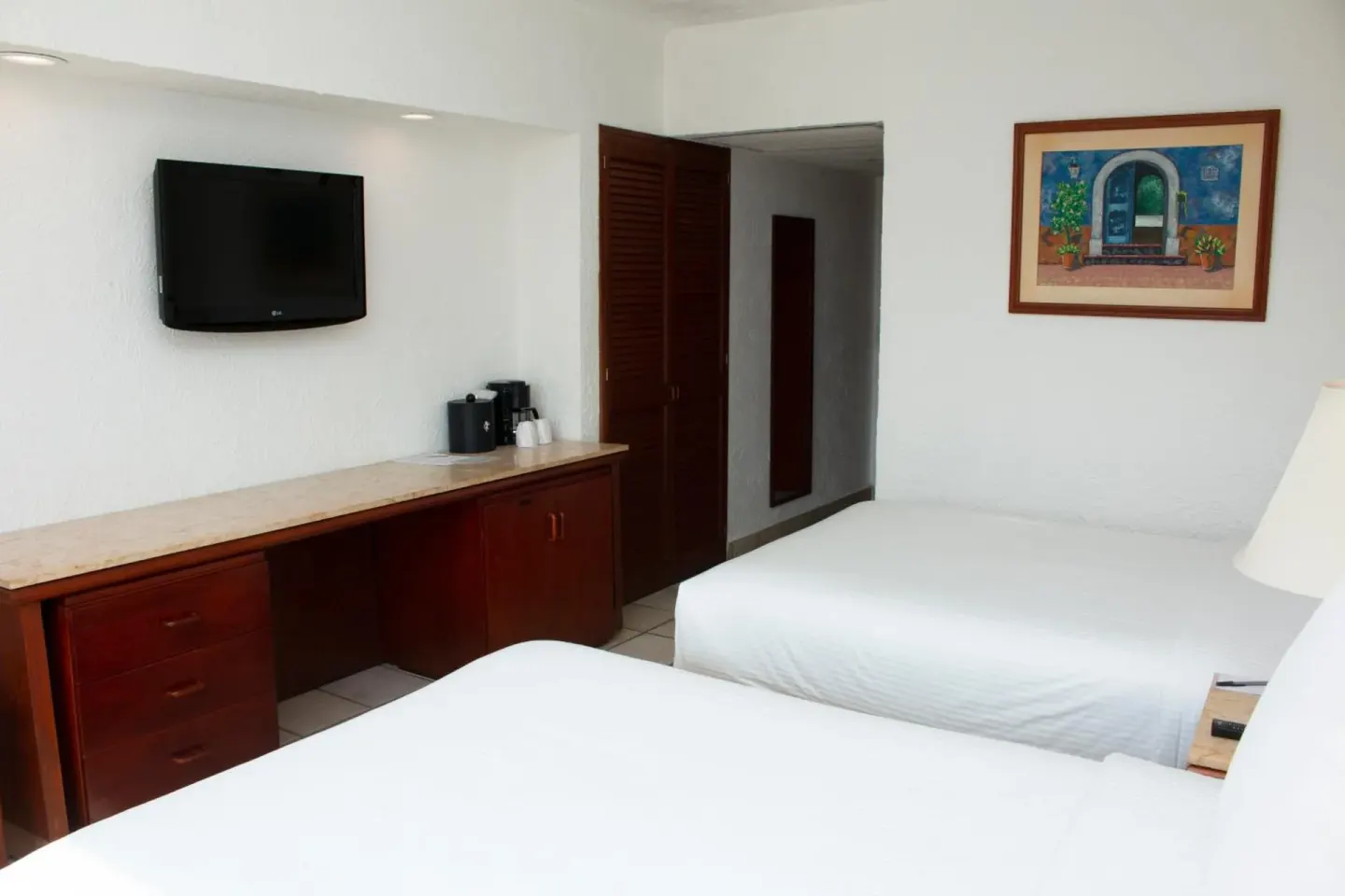 Double-bed guest room with desk, TV, and wall art at Emporio Ixtapa.