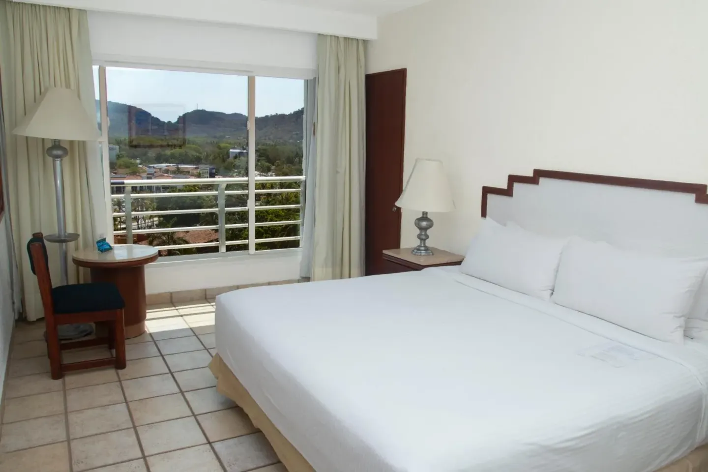King bed, small table, and hillside view in a guest room at Emporio Ixtapa.