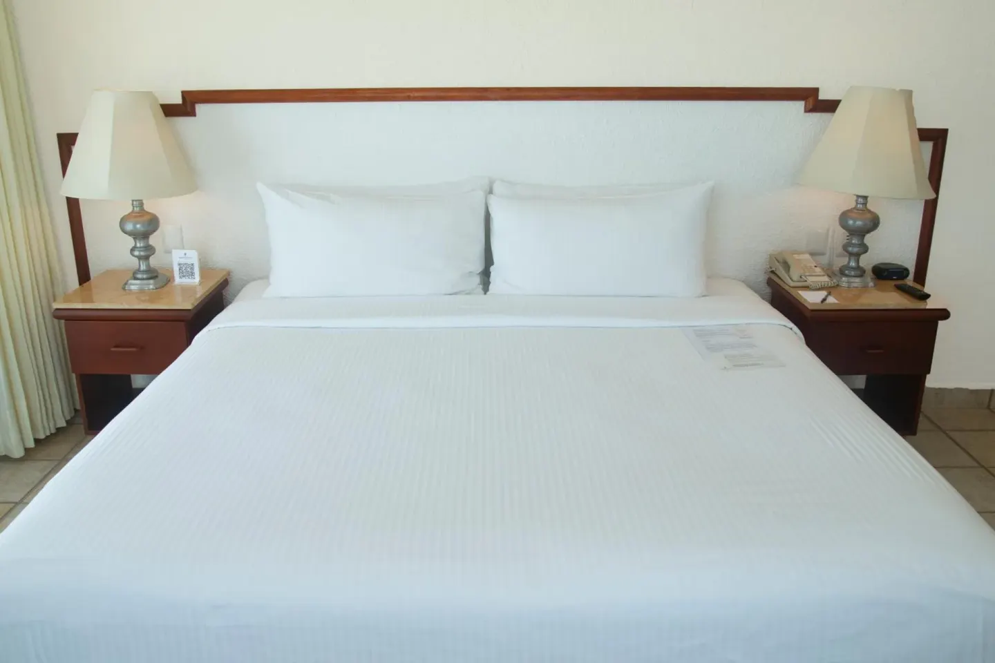 Straight-on view of a king bed with white pillows and bedside lamps at Emporio Ixtapa.