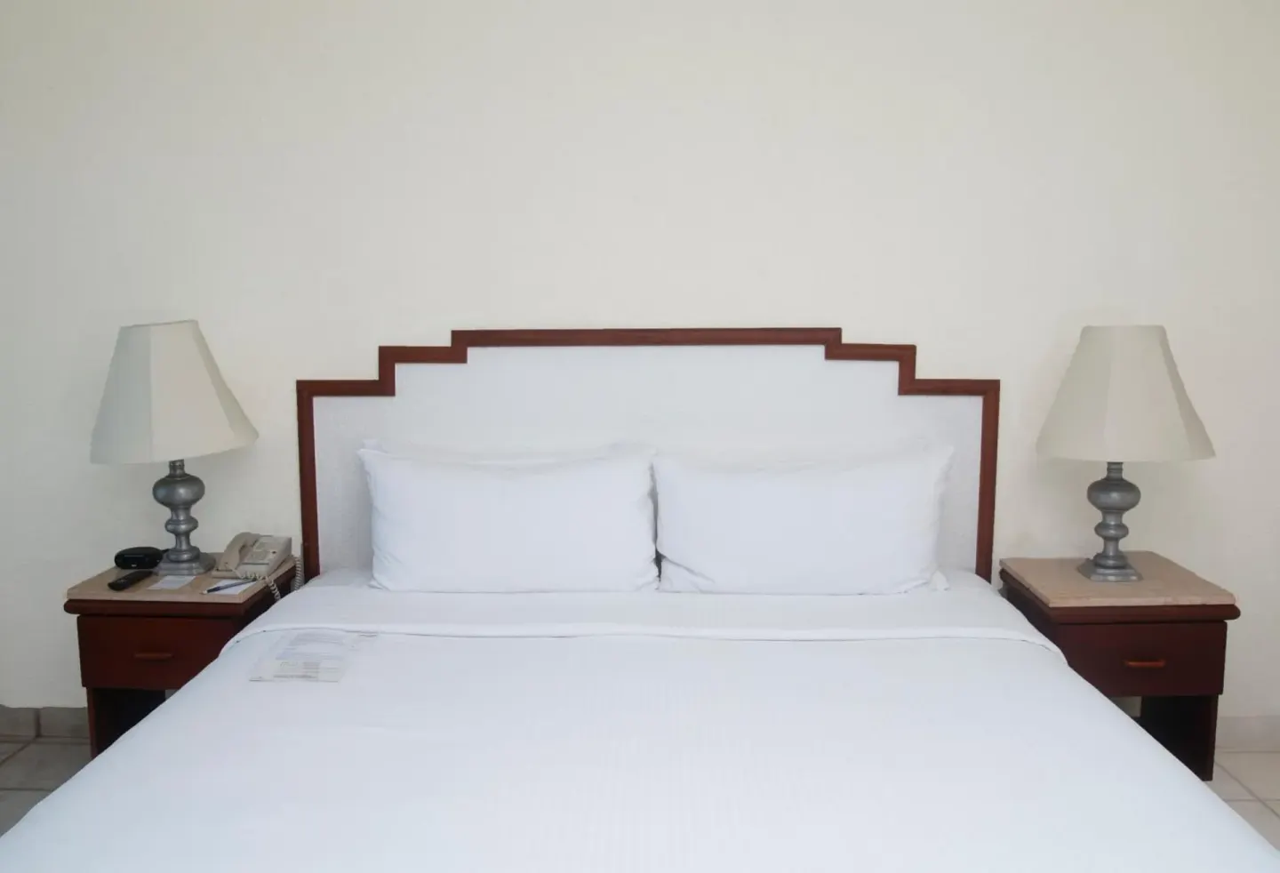 Guest room king bed with white linens and bedside lamps at Emporio Ixtapa.