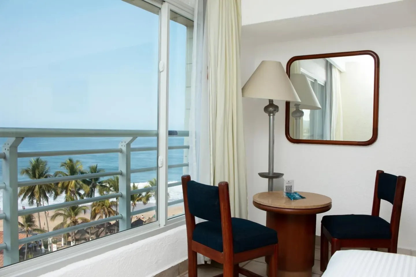 Ocean-view seating area with two chairs by the window in a guest room at Emporio Ixtapa.