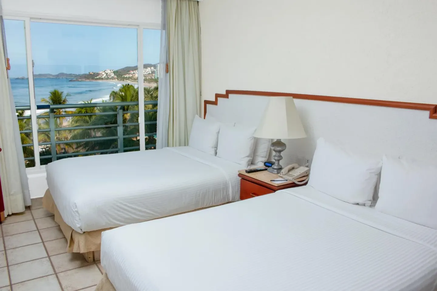 Two double beds beside a large ocean-facing window in a guest room at Emporio Ixtapa.