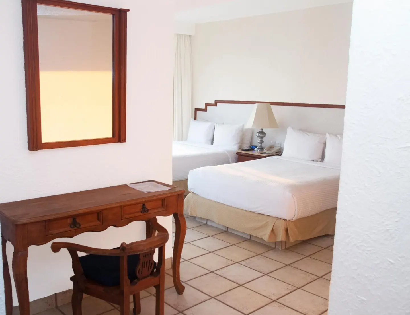 Guest room with two double beds, desk, chair and mirror at Emporio Ixtapa.