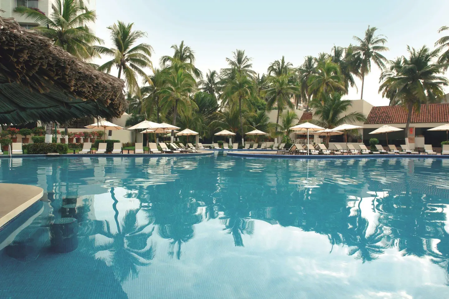 Large pool with palm reflections, loungers and umbrellas at Emporio Ixtapa.