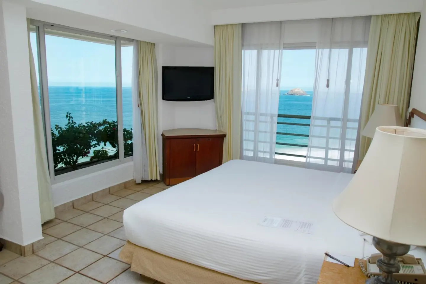 King-bed guest room with large ocean-facing windows at Emporio Ixtapa.