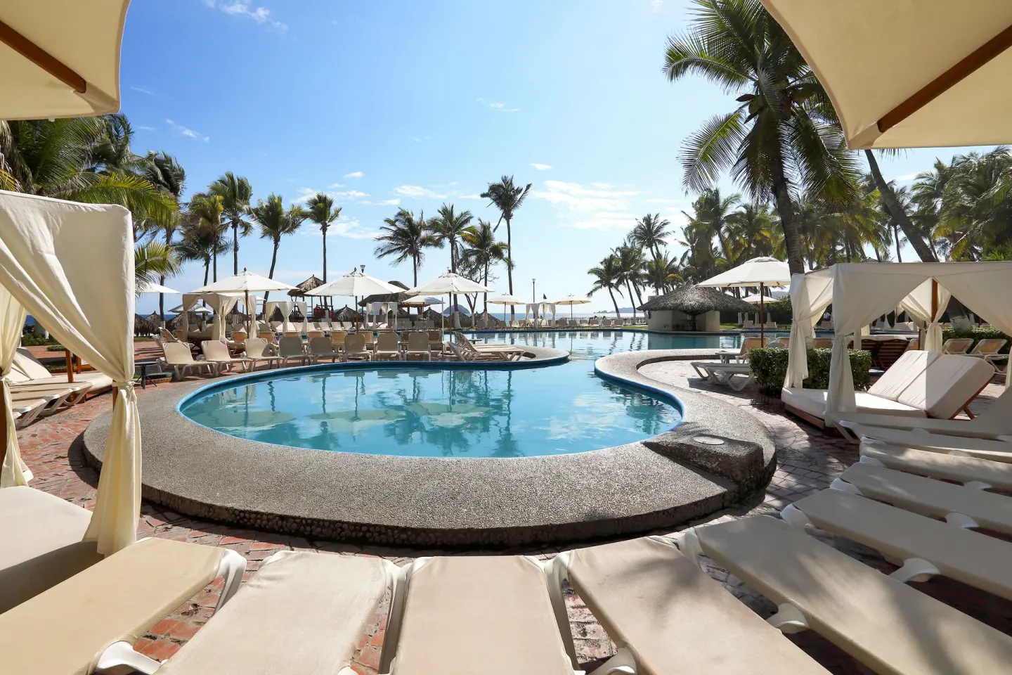 Curved pool with loungers, cabanas, umbrellas and palms at Emporio Ixtapa.