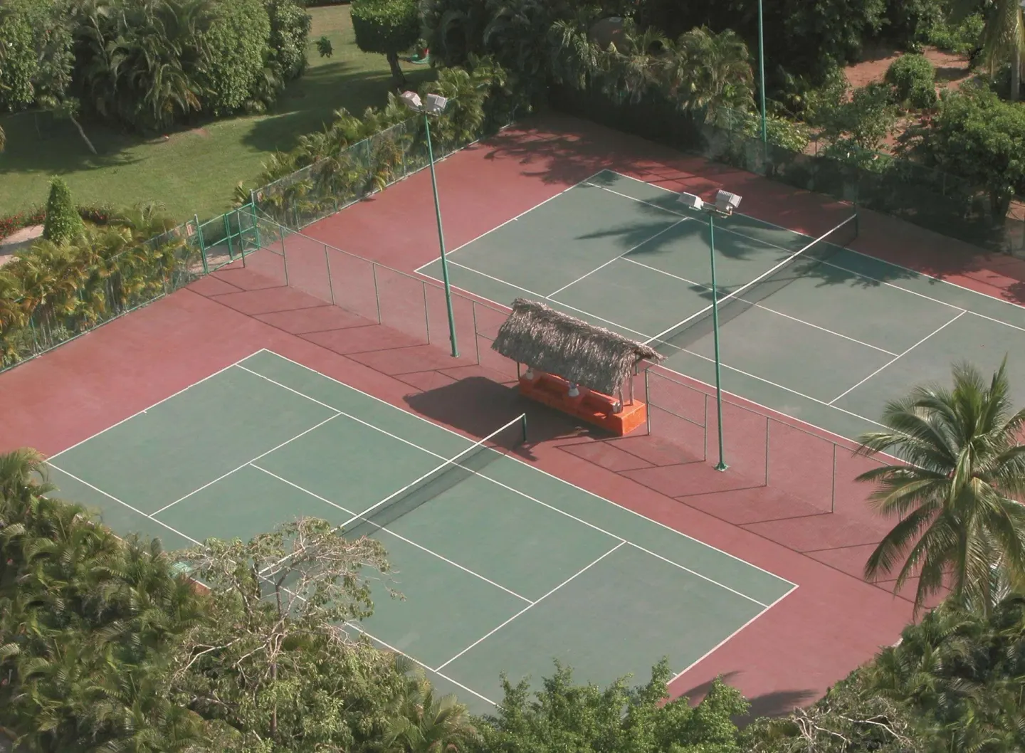 Aerial view of tennis courts with a shaded bench area at Emporio Ixtapa.