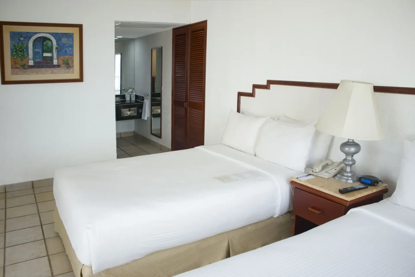 Junior Suite Ocean View bedroom with two beds and bathroom doorway at Emporio Ixtapa.