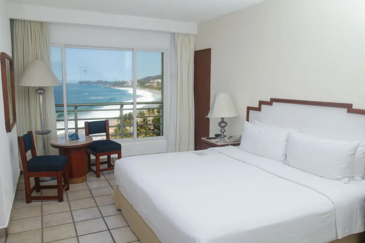 King bed in a Superior Ocean View room at Emporio Ixtapa with a beach and bay view through the window.
