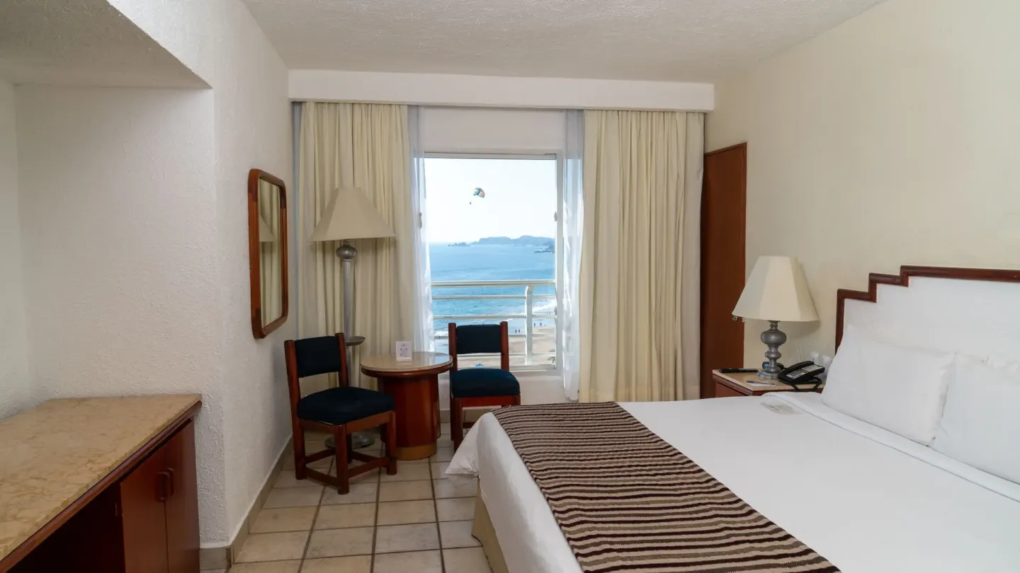 King bed and seating area in a Superior Ocean View room at Emporio Ixtapa with the sea framed by curtains.