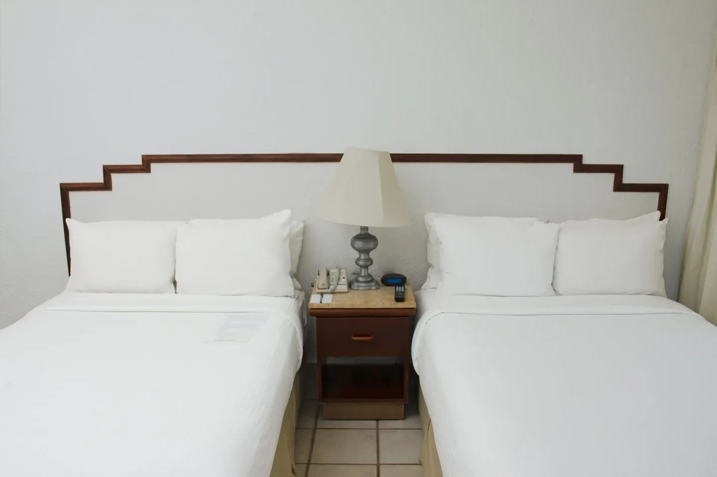 Two double beds with white linens and a shared nightstand in a guest room at Emporio Ixtapa.