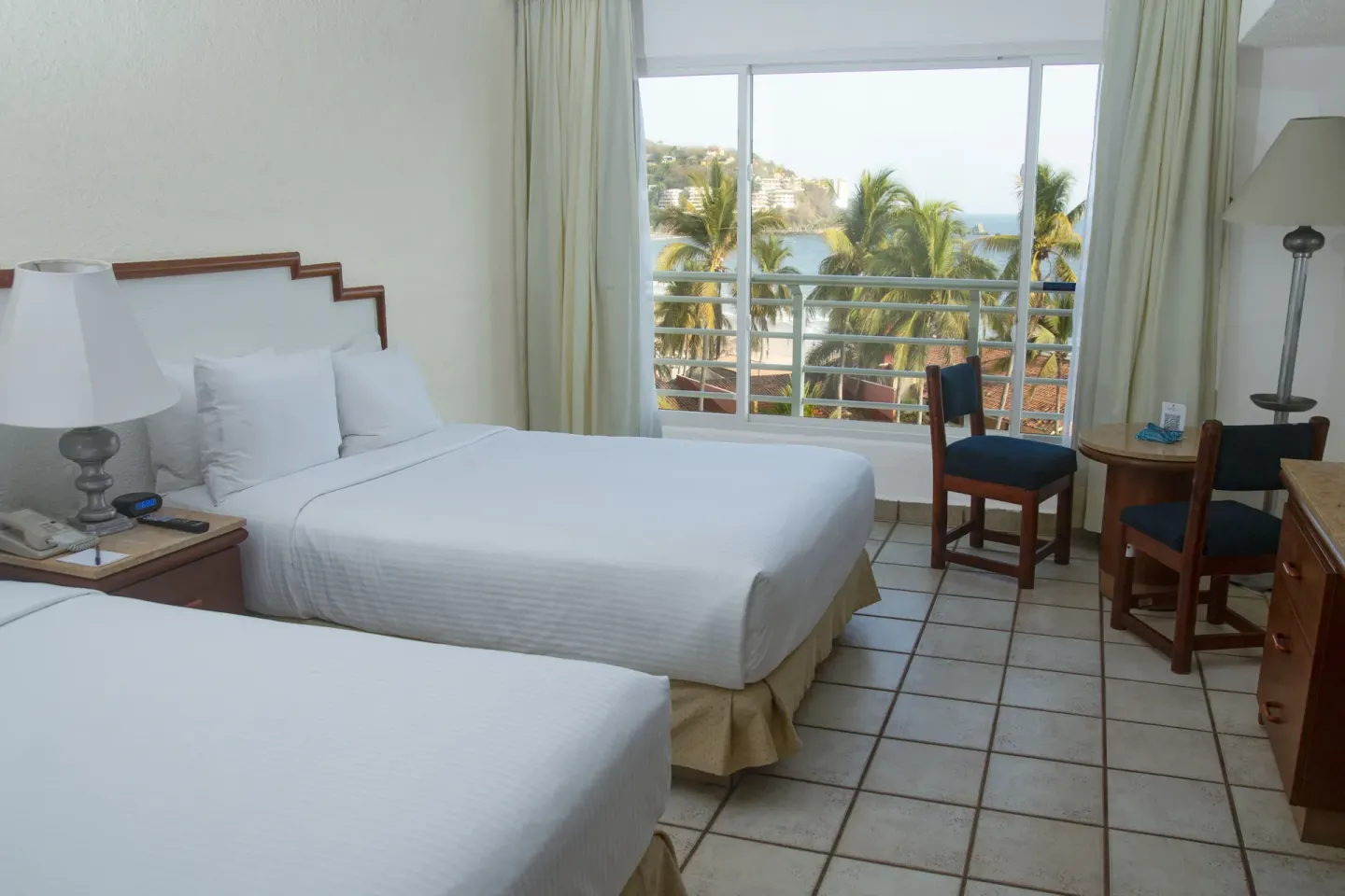 Two double beds in a Superior Ocean View room at Emporio Ixtapa with palms and sea beyond the window.