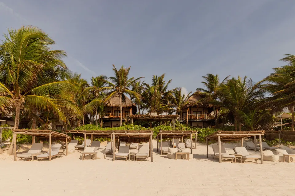 Beachfront bungalows behind a row of palapa daybeds at Encantada Tulum
