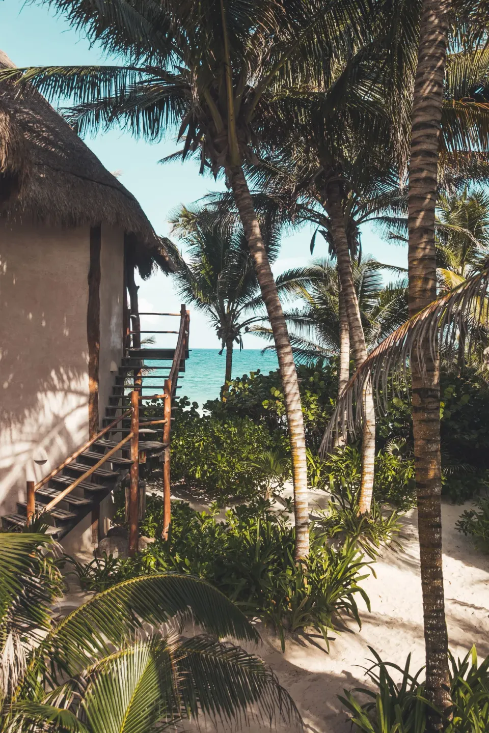 Thatched-roof bungalow and palm trees opening to the ocean at Encantada Tulum