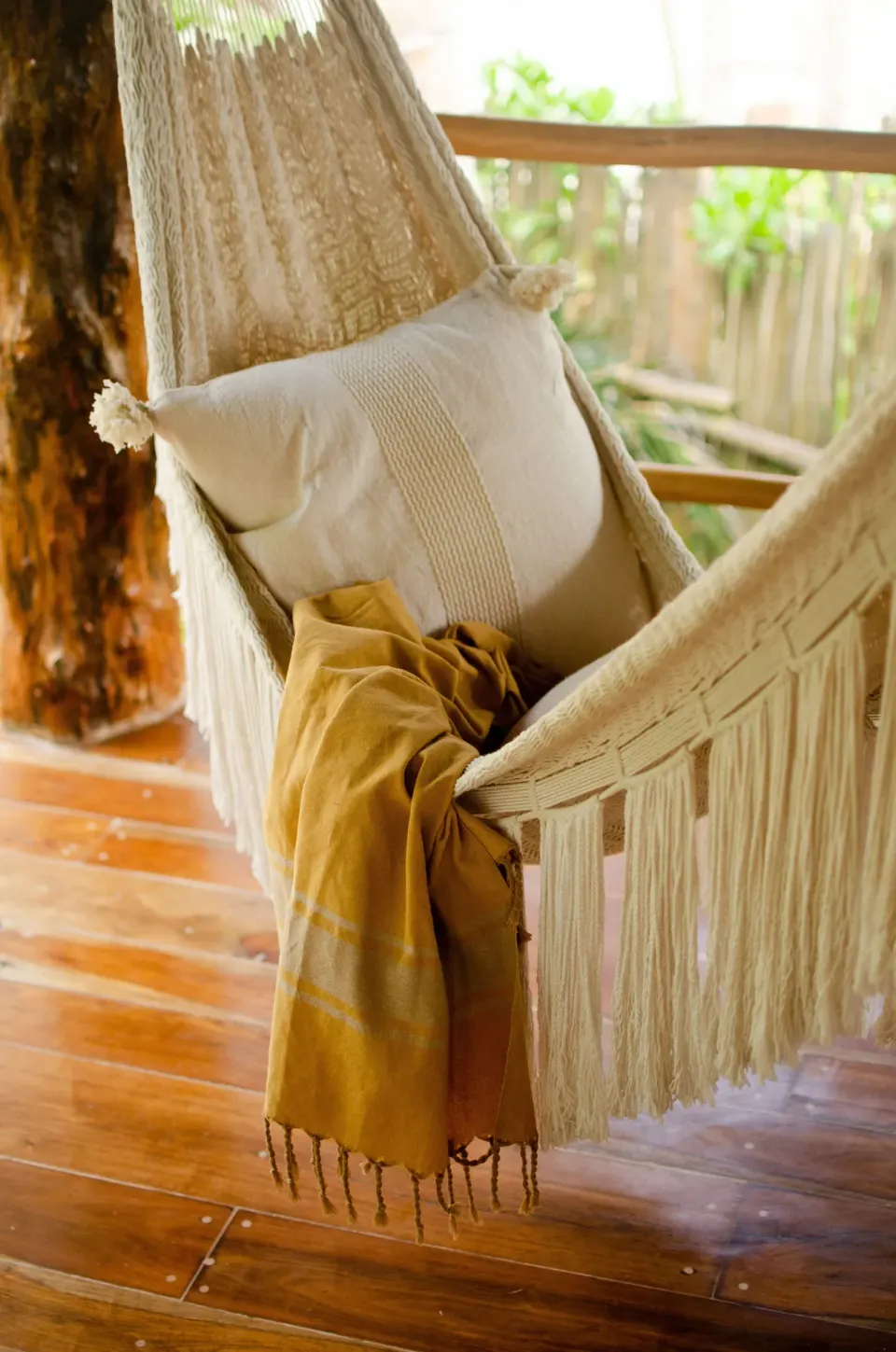 Fringed hammock with a cushion and throw draped on a wooden deck at Encantada Tulum.